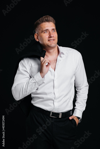 A handsome young man takes off his jacket and laughs posing on a black background. A stylish business man. A big businessman. © Andrii