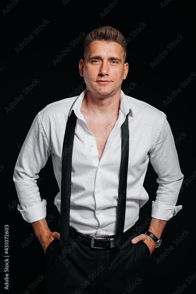 A stylish young man in a white shirt with rolled-up sleeves poses on a black background. A handsome charismatic businessman. A stylish young man in a white shirt with rolled-up sleeves poses on a black background. A handsome charismatic businessman.