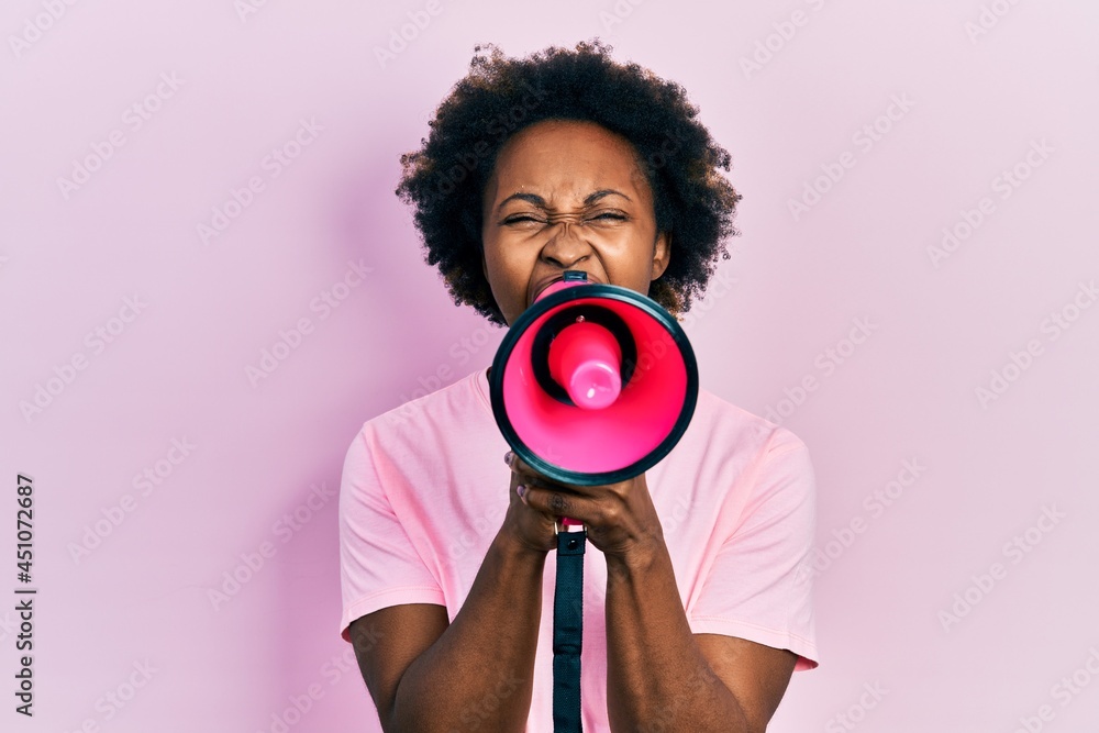 Obraz premium African american woman with afro hair screaming with megaphone over pink background
