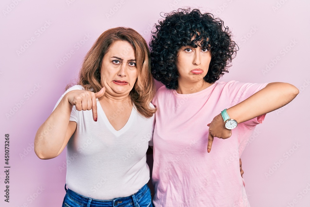 Middle east mother and daughter wearing casual clothes pointing down looking sad and upset, indicating direction with fingers, unhappy and depressed.