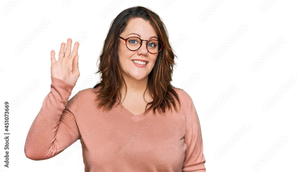 Young plus size woman wearing casual clothes and glasses waiving saying hello happy and smiling, friendly welcome gesture Young plus size woman wearing casual clothes and glasses waiving saying hello happy and smiling, friendly welcome gesture