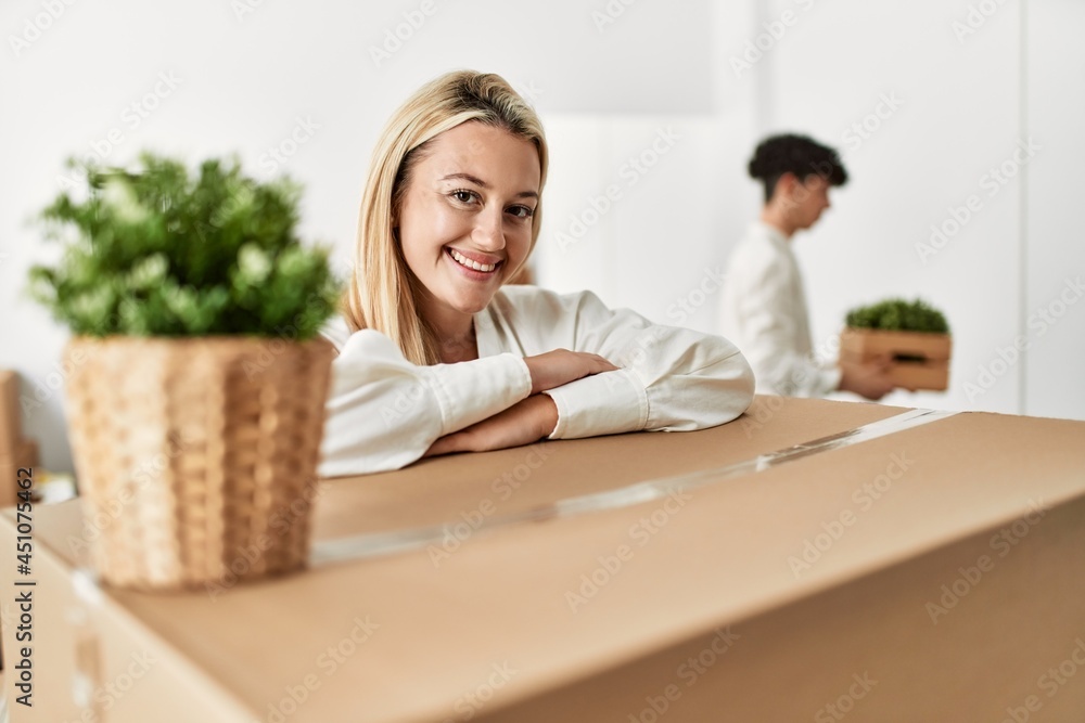 Young woman smiling happy leaning on cardboard at new home. Young woman smiling happy leaning on cardboard at new home.