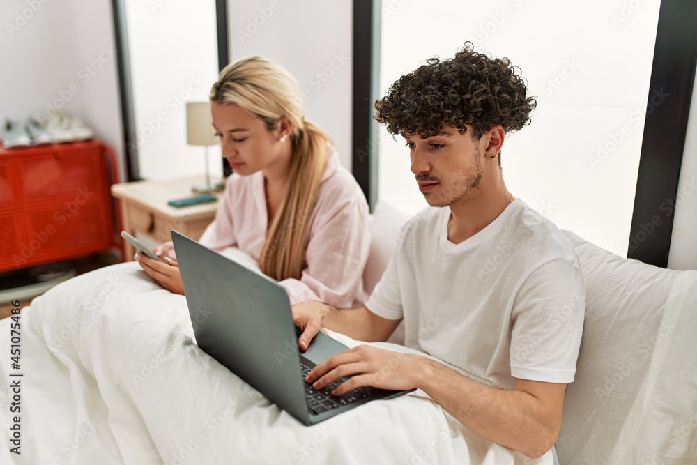 Young beautiful couple using laptop and smartphone sitting on the bed at home. Young beautiful couple using laptop and smartphone sitting on the bed at home.