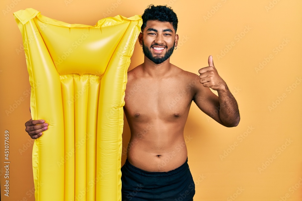 Arab man with beard wearing swimsuit and holding summer mattress float smiling happy and positive, thumb up doing excellent and approval sign Arab man with beard wearing swimsuit and holding summer mattress float smiling happy and positive, thumb up doing excellent and approval sign