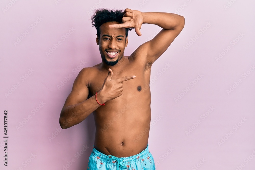 Fototapeta premium Young african american man with beard wearing swimsuit smiling making frame with hands and fingers with happy face. creativity and photography concept.
