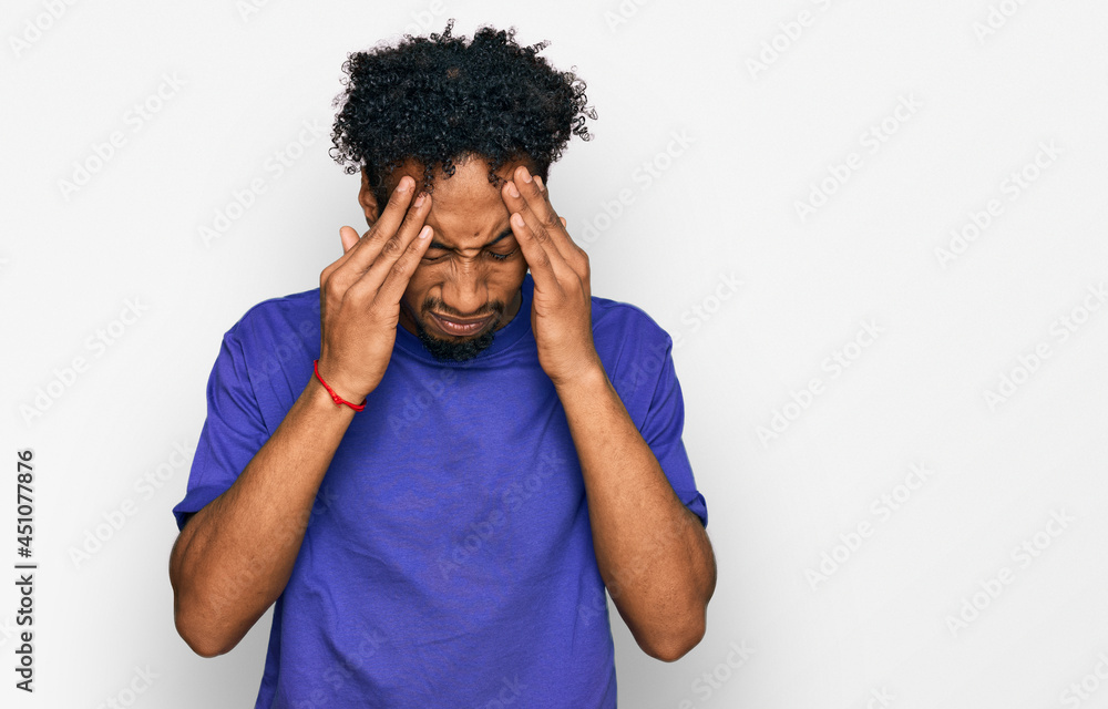 Young african american man with beard wearing casual purple t shirt with hand on head for pain in head because stress. suffering migraine. Young african american man with beard wearing casual purple t shirt with hand on head for pain in head because stress. suffering migraine.