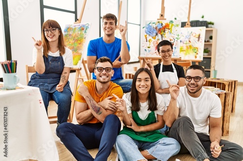 Group of people sitting at art studio smiling happy pointing with hand and finger to the side