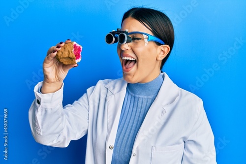 Beautiful brunette jeweller woman holding geode stone wearing magnifier glasses smiling and laughing hard out loud because funny crazy joke.