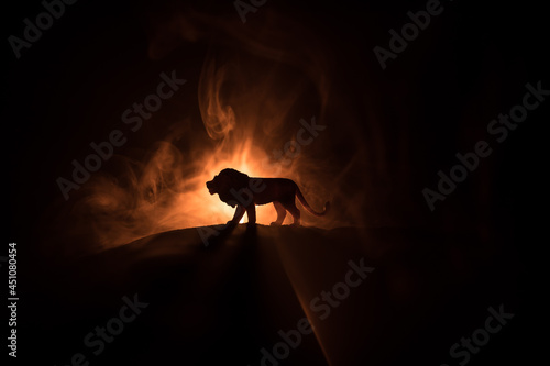 A silhouette of lion miniature standing on wooden table. Creative decoration with colorful backlight with fog. Selective focus