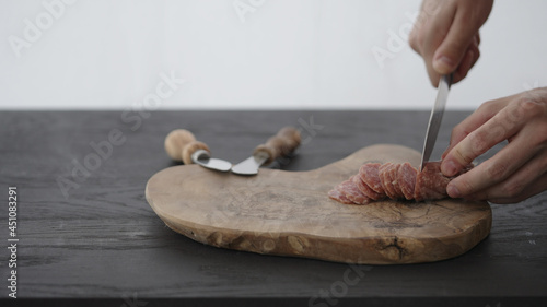 Man slcing small cured sausage on olive board with copy space photo