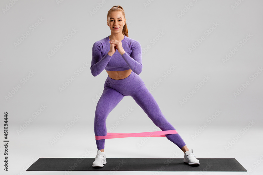 Fitness woman doing exercise for glutes with resistance band on gray background. Athletic girl working out Fitness woman doing exercise for glutes with resistance band on gray background. Athletic girl working out