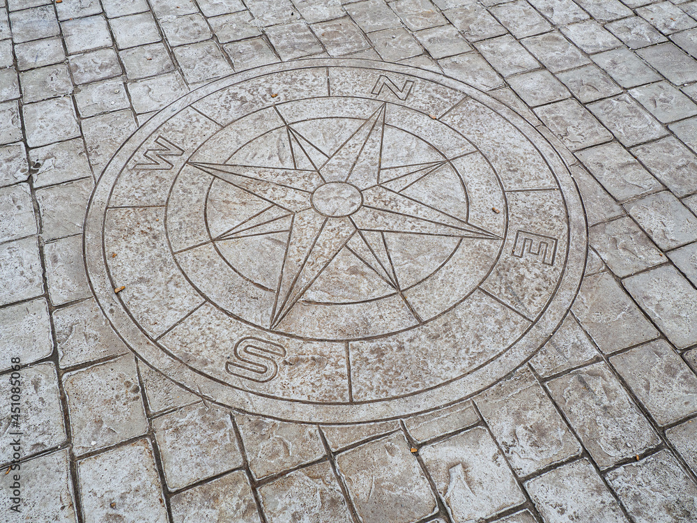 Símbolo de una brújula en el suelo adoquinado de una calle del pueblo del norte de España, verano de 2020