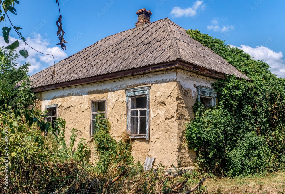 Old broken adobe rural house overgrown with wild hops