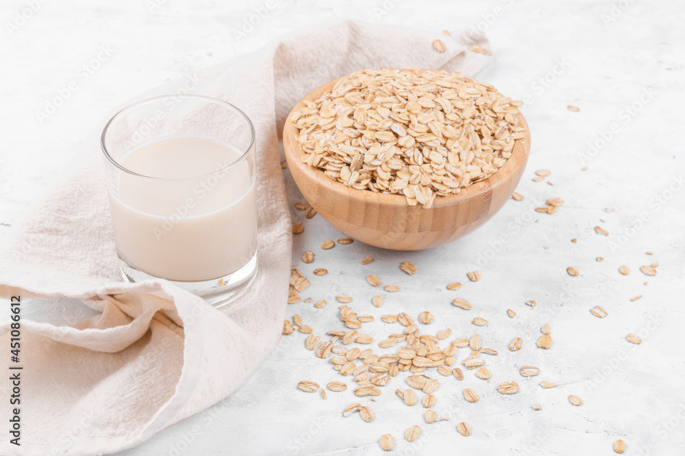 Vegan non dairy alternative milk. Glass with oat milk and a bowl with oat flake on white stone table, close up Vegan non dairy alternative milk. Glass with oat milk and a bowl with oat flake on white stone table, close up