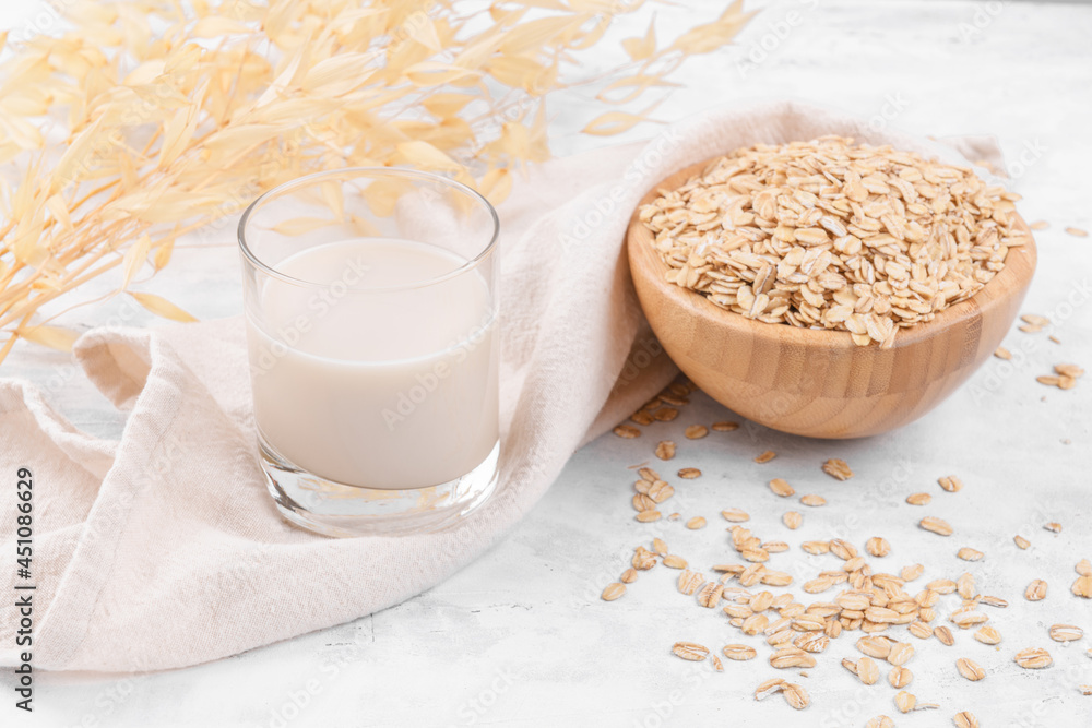 Vegan non dairy alternative milk. Glass with oat milk and a bowl with oat flake on white stone table, close up Vegan non dairy alternative milk. Glass with oat milk and a bowl with oat flake on white stone table, close up