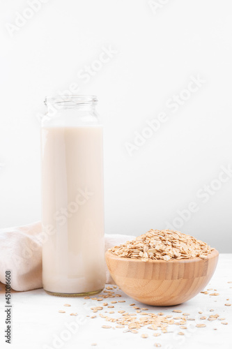 Vegan non dairy alternative milk. Oat milk in a bottle and a bowl with oat flake on white table background, copy space