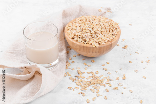 Vegan non dairy alternative milk. Glass with oat milk and a bowl with oat flake on white stone table, close up