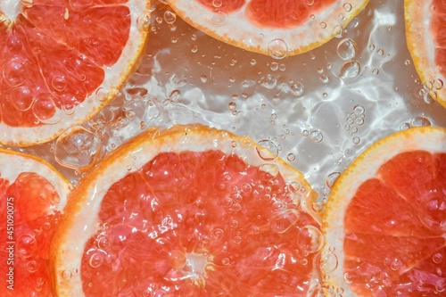 Close-up fresh slices of red grapefruit on white background. Slices of grapefruit in sparkling water on white background, closeup. Citrus soda. Copy space