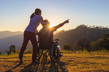 Disabled handicapped young man in wheelchair walking with his care helper in sunset.Silhouette