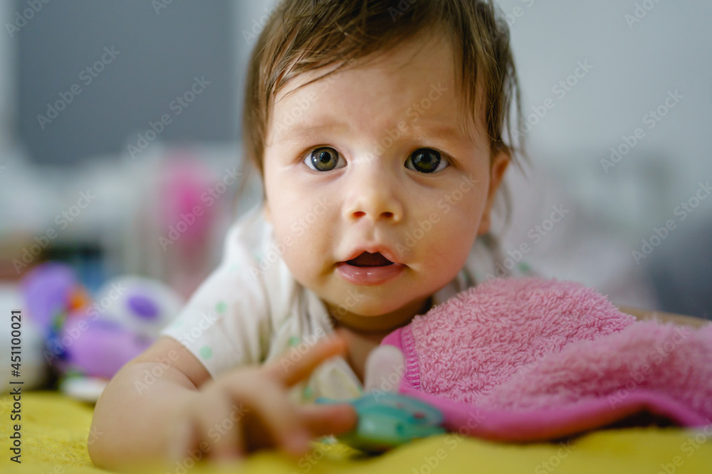 Close up portrait of small caucasian baby girl four months old front view lying on the bed at home in the evening alone Close up portrait of small caucasian baby girl four months old front view lying on the bed at home in the evening alone