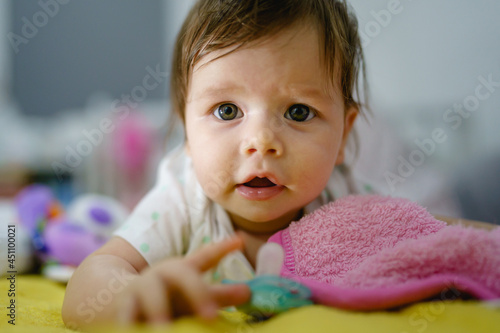 Close up portrait of small caucasian baby girl four months old front view lying on the bed at home in the evening alone