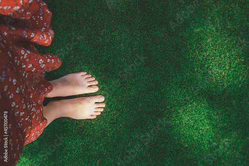 women bare feet on flat green grass lawn, top view. woman dressed in red dress. walking with bare feet on natural textures. selective focus