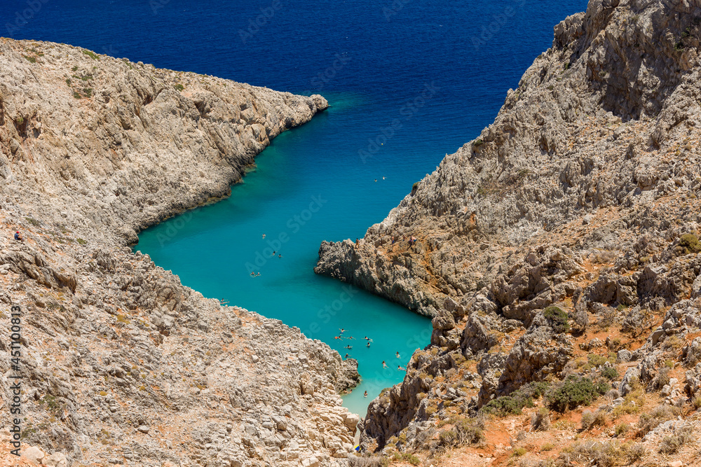 Small sandy beach with turquoise ocean hidden between tall cliffs in a narrow canyon (Seitan Limania, Crete)
