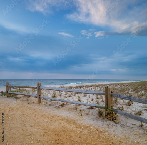 beach summer sand and wood fenced sand dunes with white clouds  blue sky and ocean waves