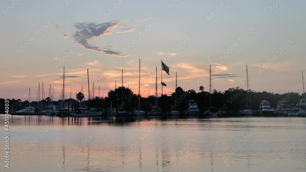 Sunrise over a seaside or lakeside marina with sailboats and an American flag flying Sunrise over a seaside or lakeside marina with sailboats and an American flag flying