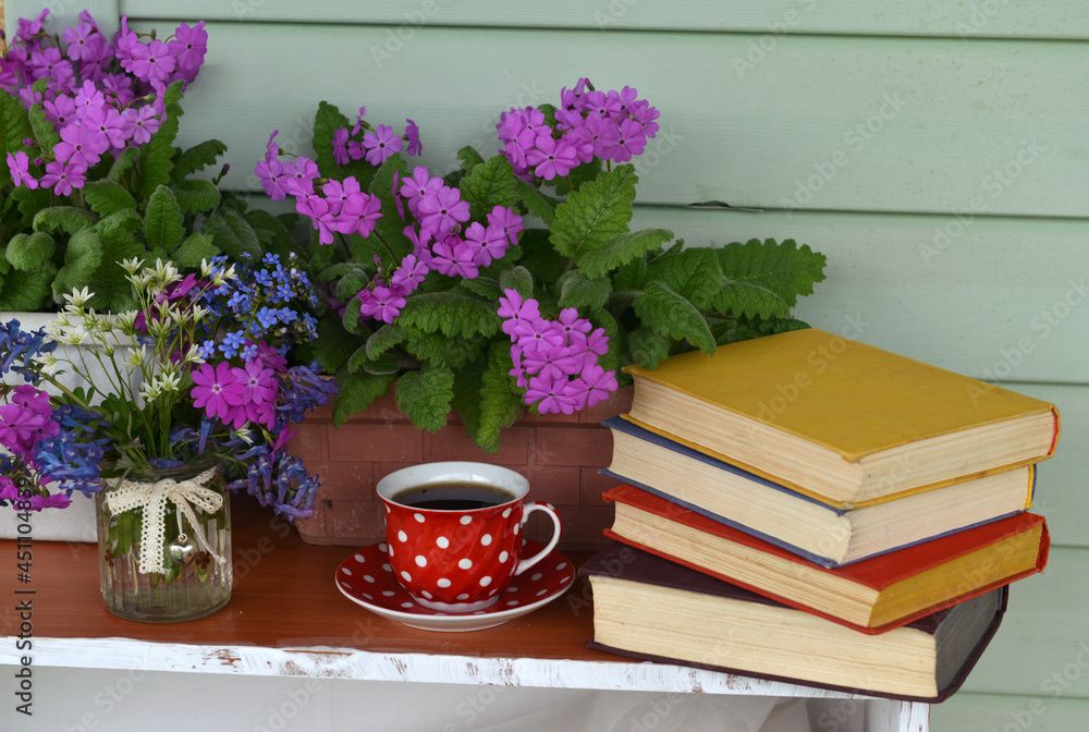 Still life with spring flowers in pot, cup of tea and books with colorful covers.