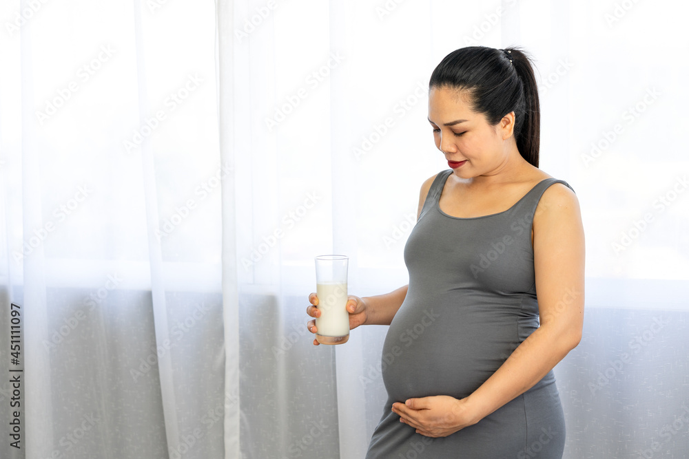 Asian pregnant women holding glass of calcium milk, drinking healthy vitamins and holding her belly. Modern healthy mom concept Asian pregnant women holding glass of calcium milk, drinking healthy vitamins and holding her belly. Modern healthy mom concept