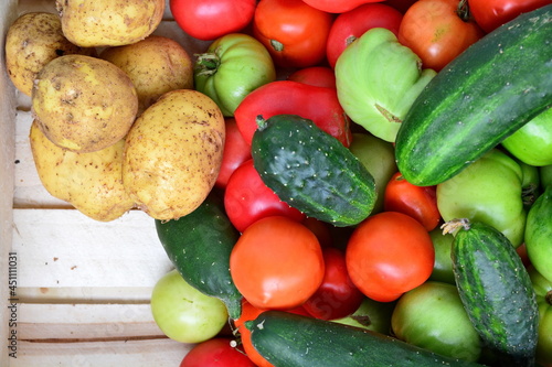 Vegetables in a wooden box. Heap of natural red and green tomatoes  yellow fresh tuber of potatoes and cucumbers on the boards. Top view  copy space