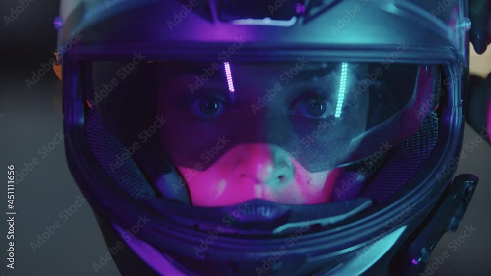A woman takes off her motorcycle helmet in neon lighting A woman takes off her motorcycle helmet in neon lighting
