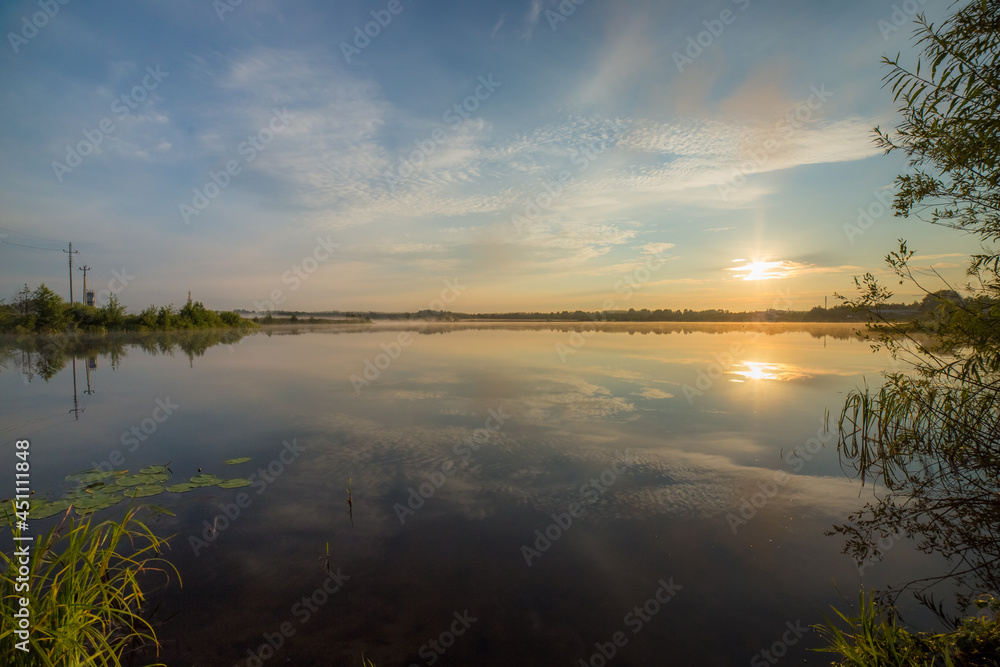 Fototapeta premium the mirror surface of the lake reflects the rising sun and the surrounding landscape on a beautiful summer morning