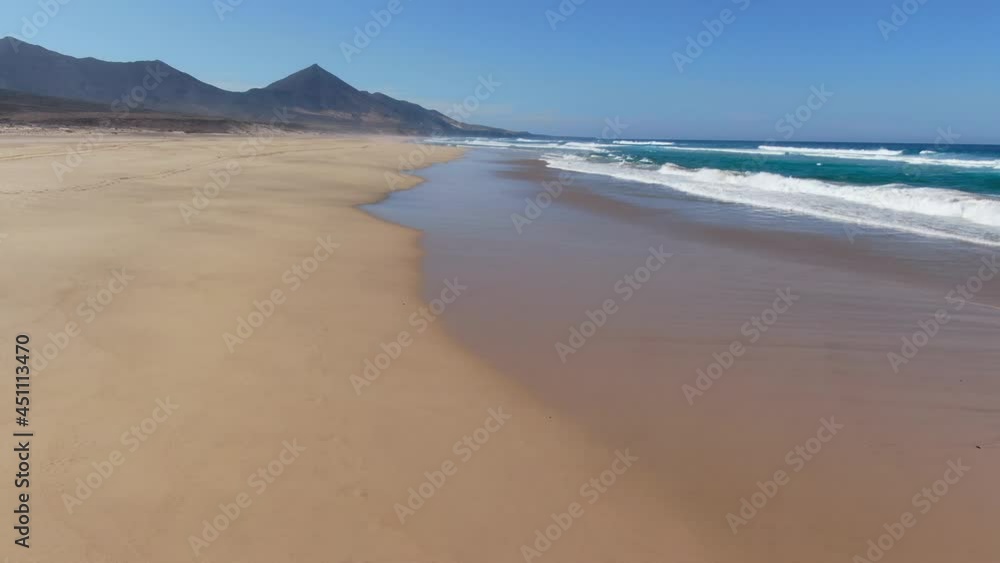Low altitude drone flight over a deserted sandy paradise beach with blue waves. Beautiful mountains in background. Low altitude drone flight over a deserted sandy paradise beach with blue waves. Beautiful mountains in background.