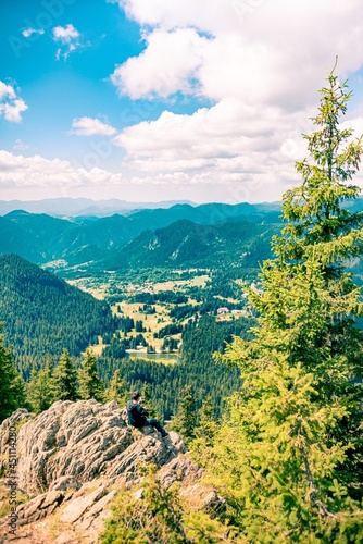 Obraz na płótnie An young man sitting at the end of a rock, looking at the magnificent mountain aria view. w salonie