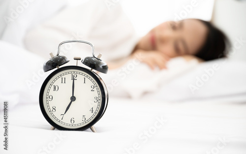 Young asian woman happy sleep at morning in bedroom. Closeup of alarm clock on white bed