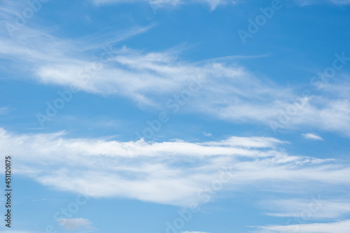 Real Soft Textured Feathery Clouds In Blue Sky Background. On a summer day, feathery fluffy clouds of various shapes and sizes slowly float across the light blue sky.