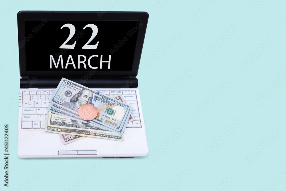 Laptop with the date of 22 march and cryptocurrency Bitcoin, dollars on a blue background. Buy or sell cryptocurrency. Stock market concept. Laptop with the date of 22 march and cryptocurrency Bitcoin, dollars on a blue background. Buy or sell cryptocurrency. Stock market concept.