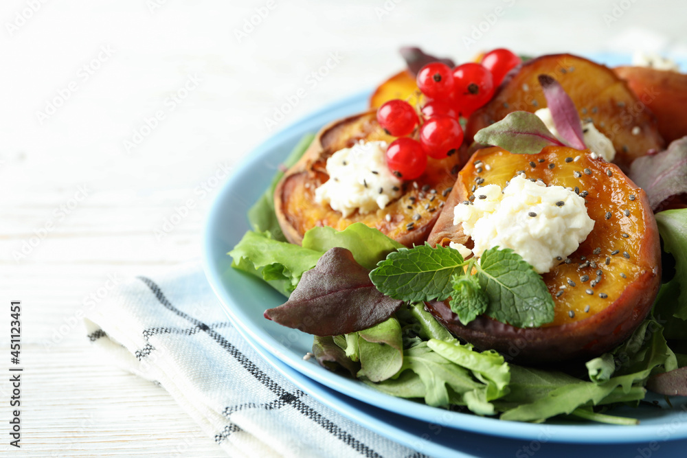 Plate of salad with grilled peach on white wooden table
