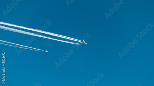 A pair of planes flying next to each other. A huge passenger airliner and a small plane. Traces of jet engines against the blue sky. The flight of planes. Travel by plane. The plane flies over the cit