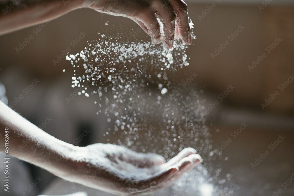 Fototapeta premium Girl scattering flour in the air, close-up photo of hands