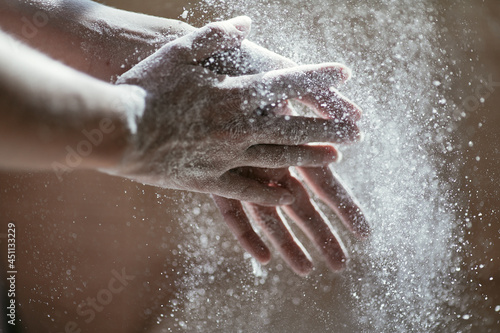 Girl shaking hands off flour, close-up photo of hands in backlight, blurred background