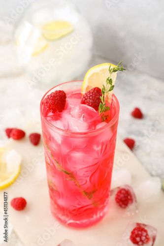 Glass of tasty raspberry lemonade on light background