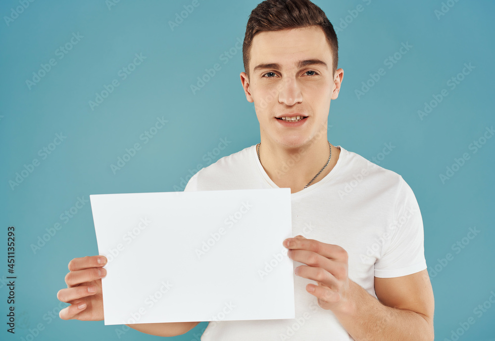 handsome man in white t-shirt with white sheet of paper in his hands paperspace blue background handsome man in white t-shirt with white sheet of paper in his hands paperspace blue background