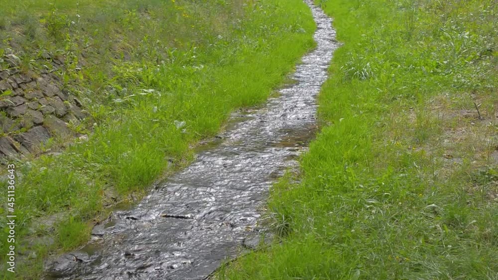 Small natural stream brook water in meadow grass on stone ground bed Small natural stream brook water in meadow grass on stone ground bed