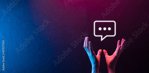 Hand on neon background holding a message icon, bubble talk notification sign in his hands. Chat icon, sms icon, comments icon, speech bubbles photo