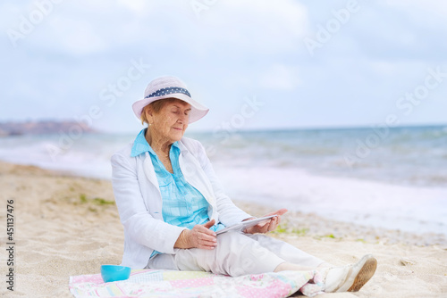 Very old wrinkled woman with a laptop on the seashore. 