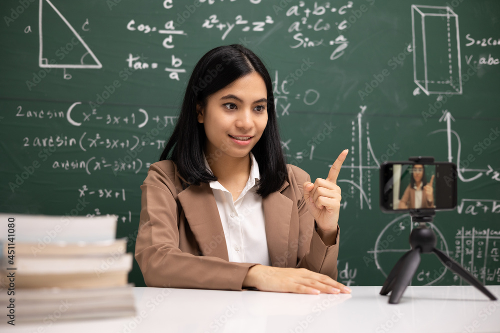 Young asian teacher woman sitting and video conference with student. Female teacher training the mathematics in classroom from live stream with smartphone online course.