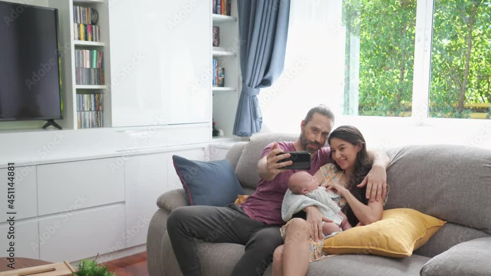 Caucasian husband use smartphone taking selfie or video call with his wife and sleeping newborn baby son in home living room. Happy family father and mother with infant child boy relationship concept Caucasian husband use smartphone taking selfie or video call with his wife and sleeping newborn baby son in home living room. Happy family father and mother with infant child boy relationship concept